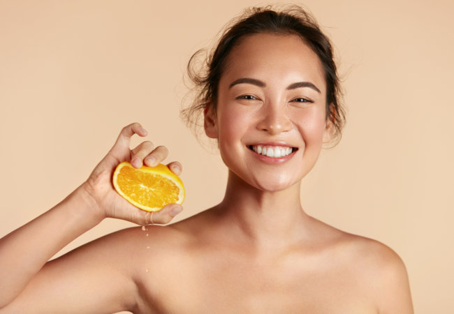 Woman with radiant face skin squeezing orange